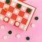 up close editorial image of pink adn red checker board with green and white pieces
