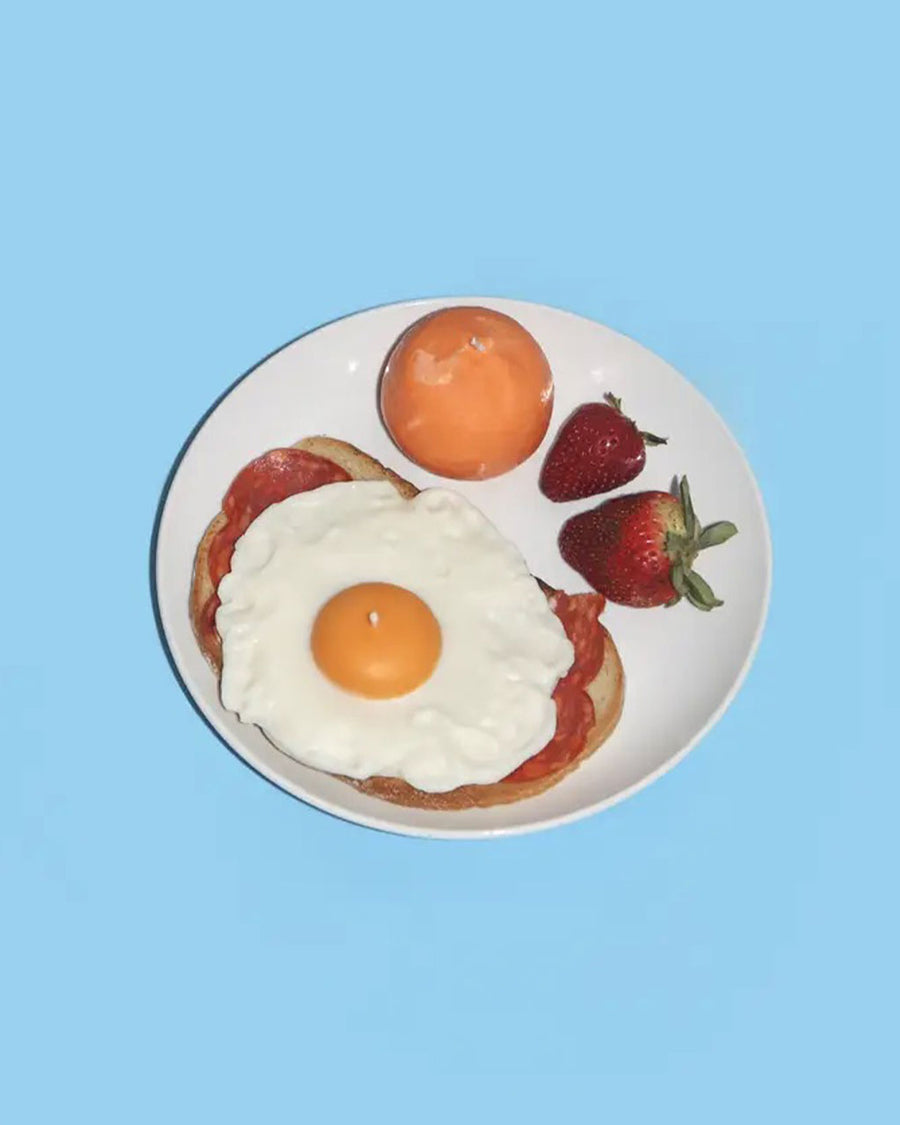 sunnyside up egg candle on a plate with an orange, strawberries and toast