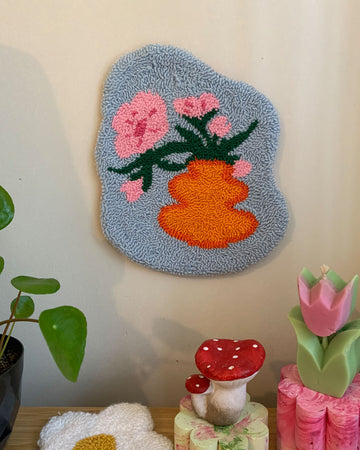 blue ground wall hanging with orange vase and floral print on wall