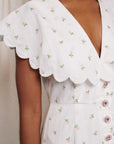 up close of model wearing midi white dress with oversized collar, pink gem buttons and all over dainty floral print