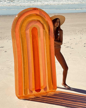 model holding curved rainbow pool float with various tones of pink, orange and red