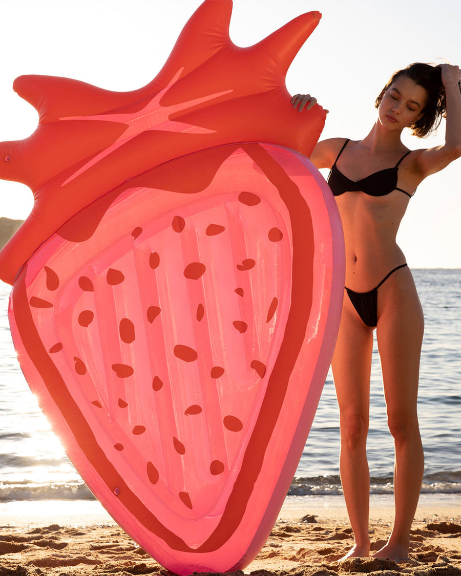 model holding orange and pink large strawberry pool float
