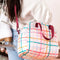 model wearing light pink puffy skate bag with multicolor plaid and burgundy strap