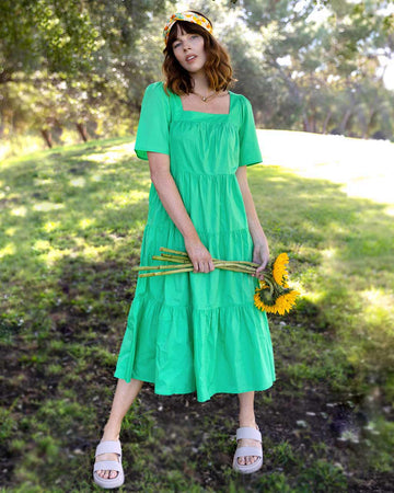 model wearing green tiered midi dress, headband, and holding sunflowers