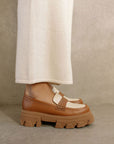 sideview of model wearing tan platform loafers with cream accents and brown soles
