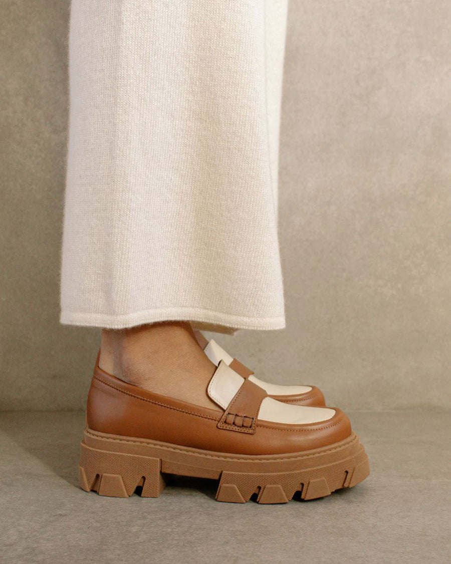 sideview of model wearing tan platform loafers with cream accents and brown soles