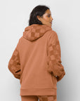 back view of model wearing terracotta colored hoodie with fleece checker pocket, sleeves, and hood and embroidered vans front
