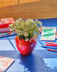 strawberry vase with white flowers on blue surface with desk accessorie scattered throughout