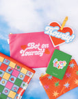 set of three carryall bags: small red with colorful starbursts, medium pink 'bet on yourself', and large clear bag with colorful checker and fun spade, heart, cherry, diamond print