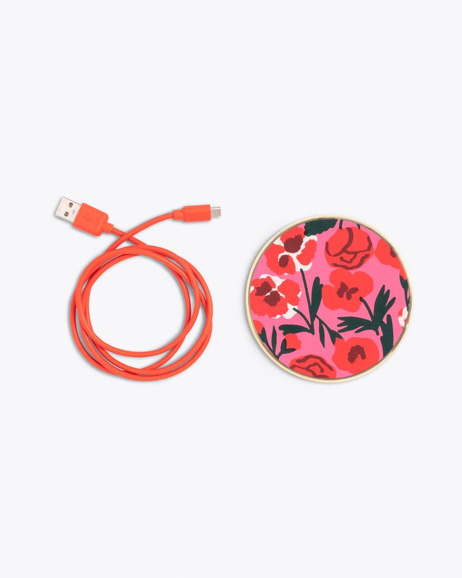 circular wireless charging pad in bold pink floral print with red charging cord coiled to the side