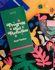 editorial image of goal tracker with pink elastic closure, dark green ground and 'progress not perfection' text and retro daisies