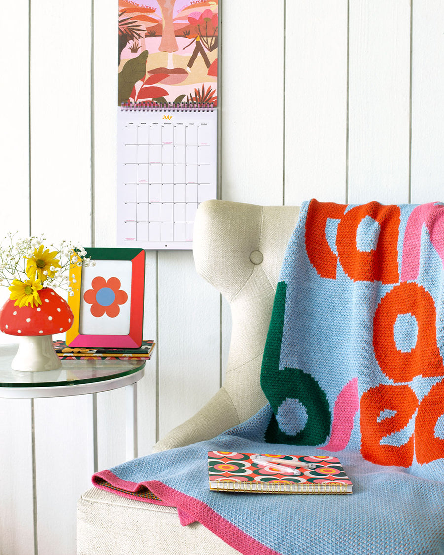 editorial image of light blue knit blanket with multicolor 'take a break' on front and pink border