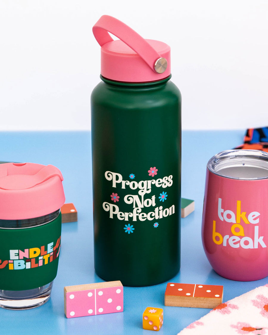 editorial image of progress not perfection stainless steel bottle, endless possibilities glass travel mug, and pink take a break stainless steel wine glass