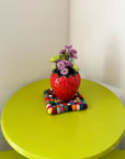strawberry vase with daisies inside and on a table