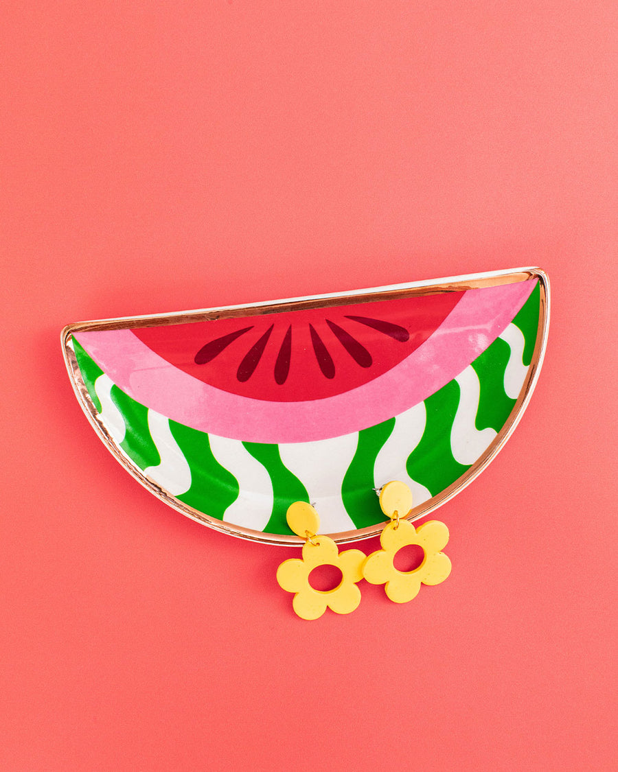 editorial image of abstract watermelon trinket tray, yellow floral earrings on a orange background
