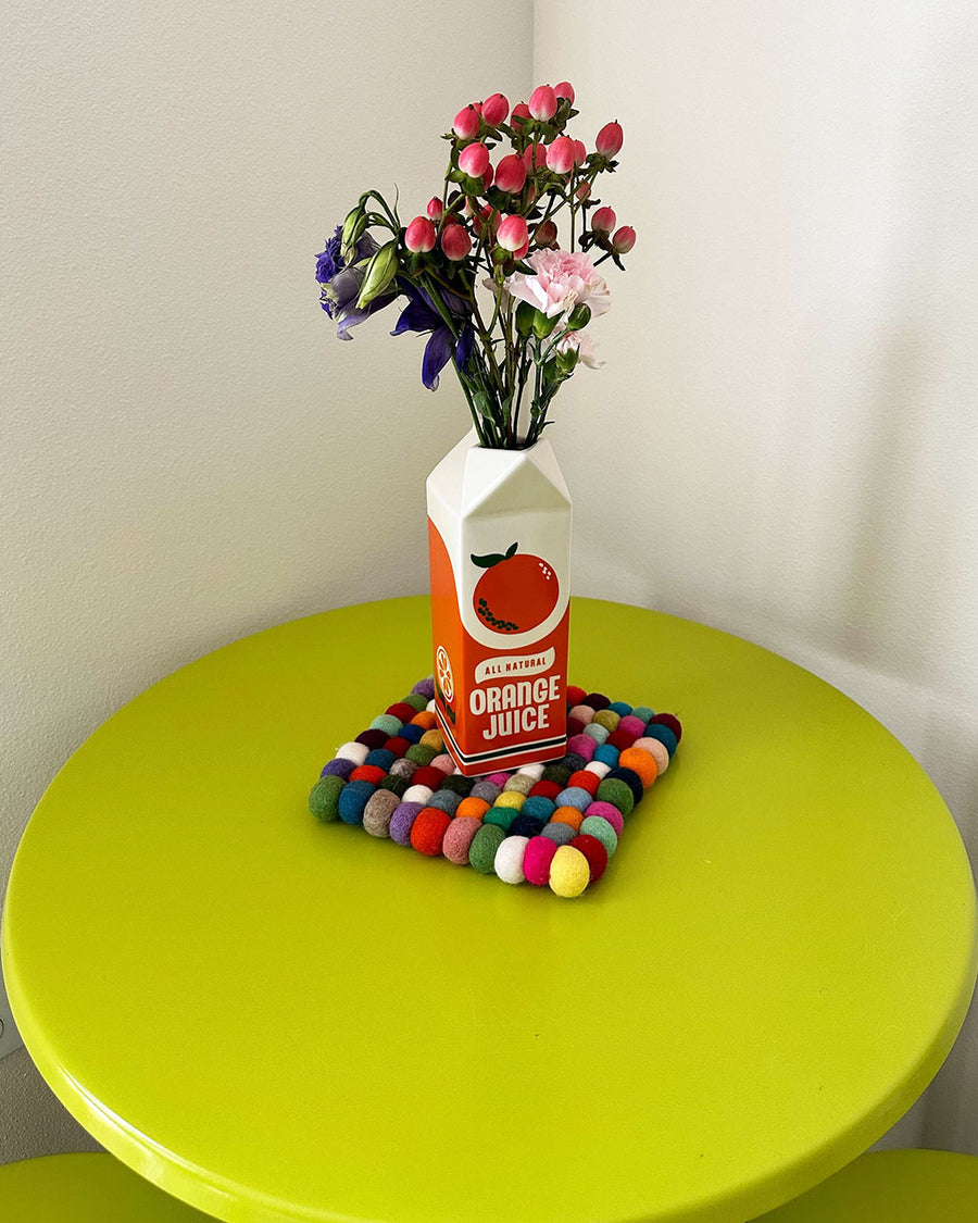 orange juice carton vase with flowers inside and on a green table
