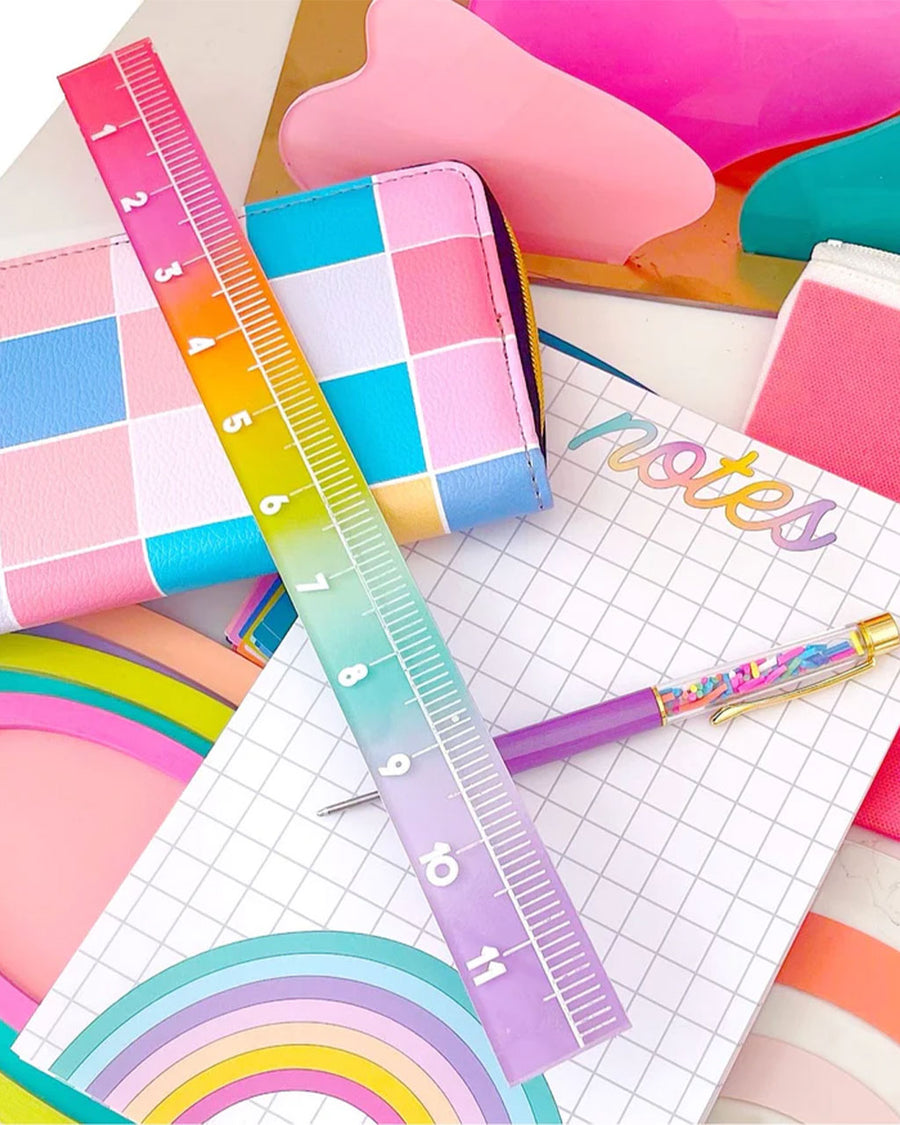 rainbow colored ruler with notepad, pen and wallet in the background